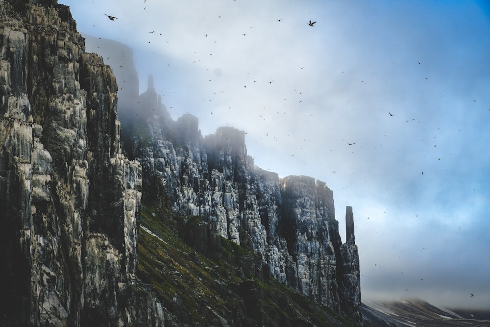 a mountain with birds flying over it on a cloudy day