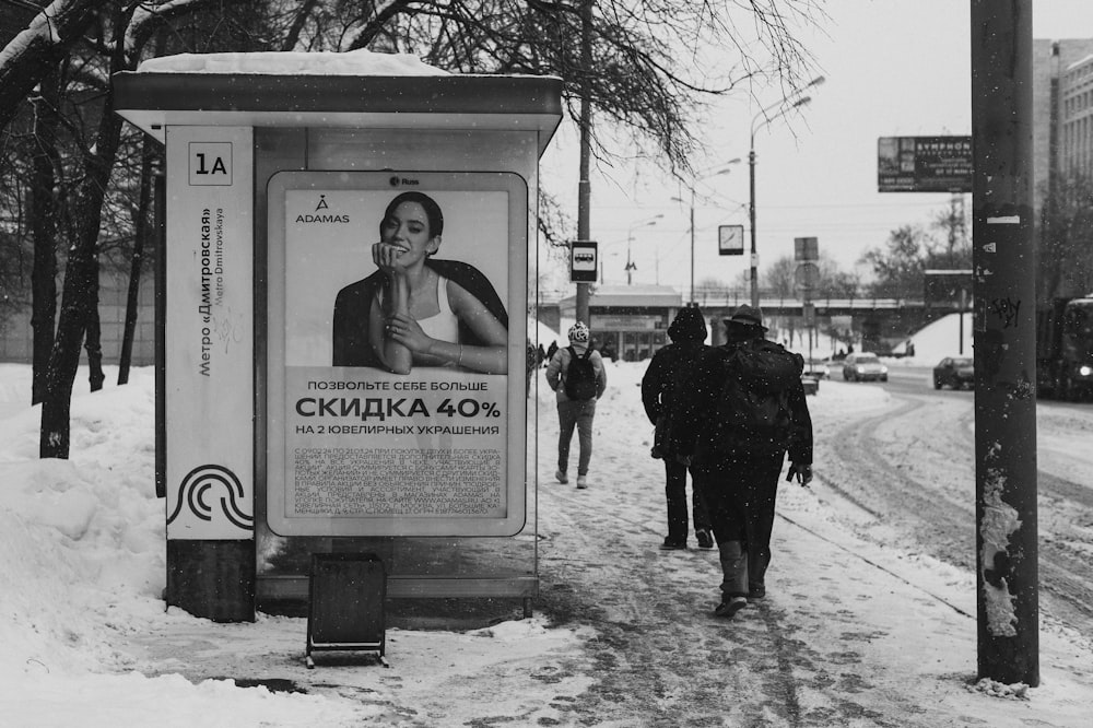 people walking down a snowy sidewalk next to a bus stop