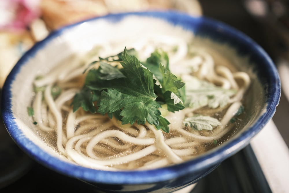 a blue and white bowl filled with noodles and cilantro