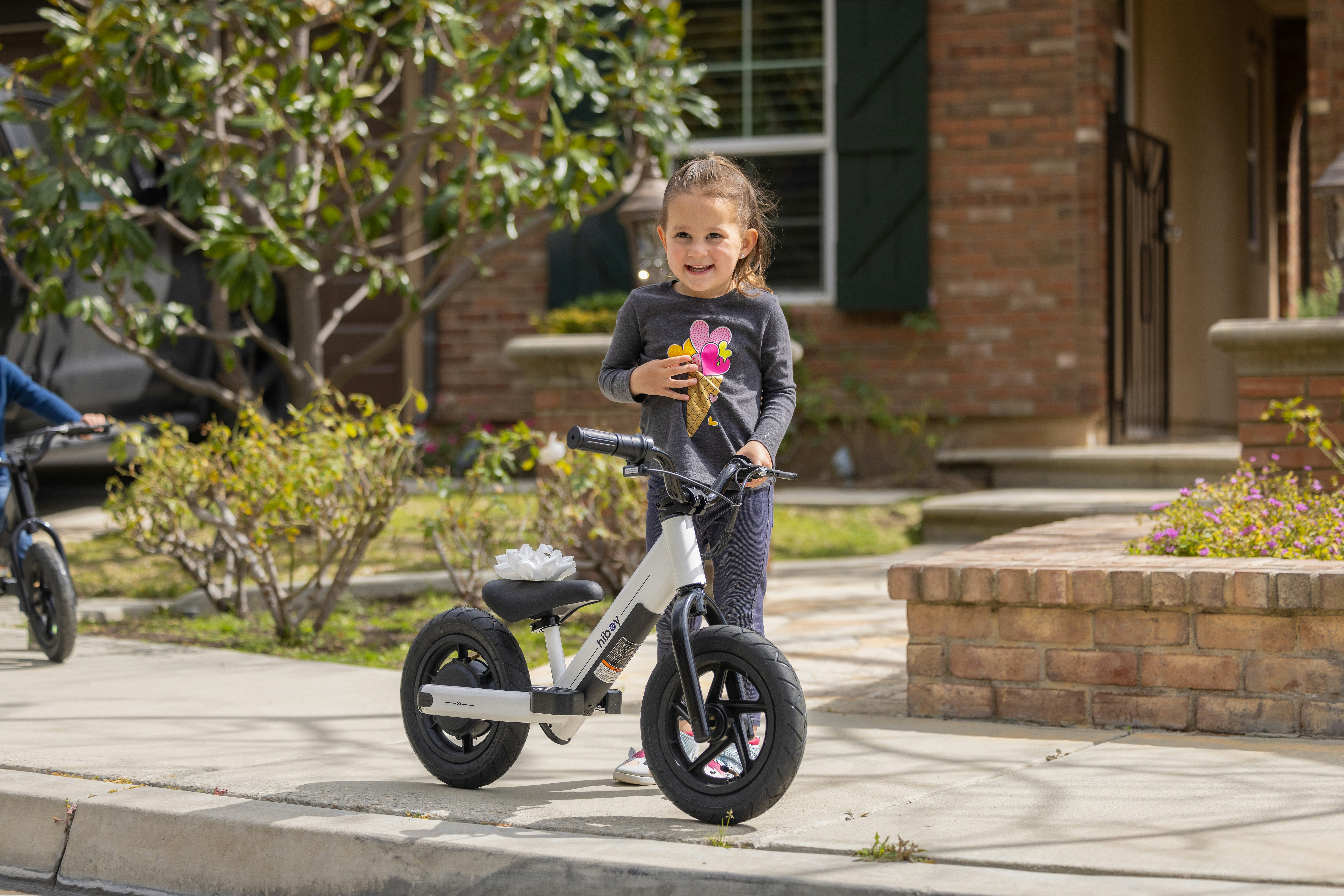 a little girl standing next to a little girl on a bike