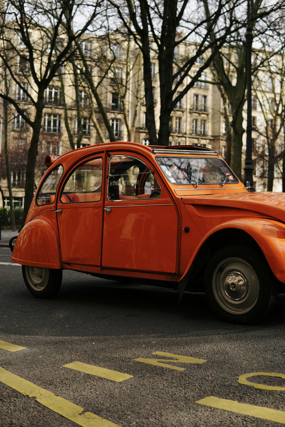 an orange car driving down a street next to tall buildings