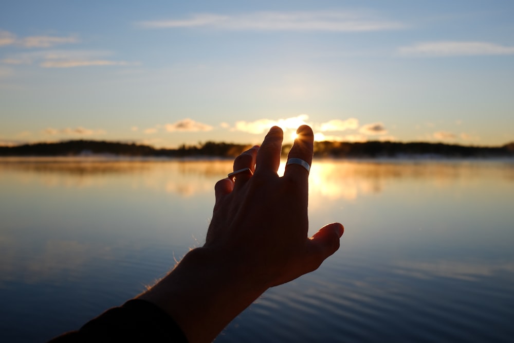a person's hand reaching for the sun over a body of water