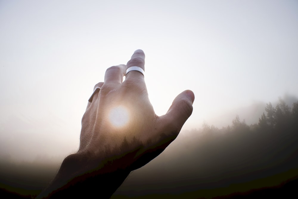a person's hand reaching up towards the sun