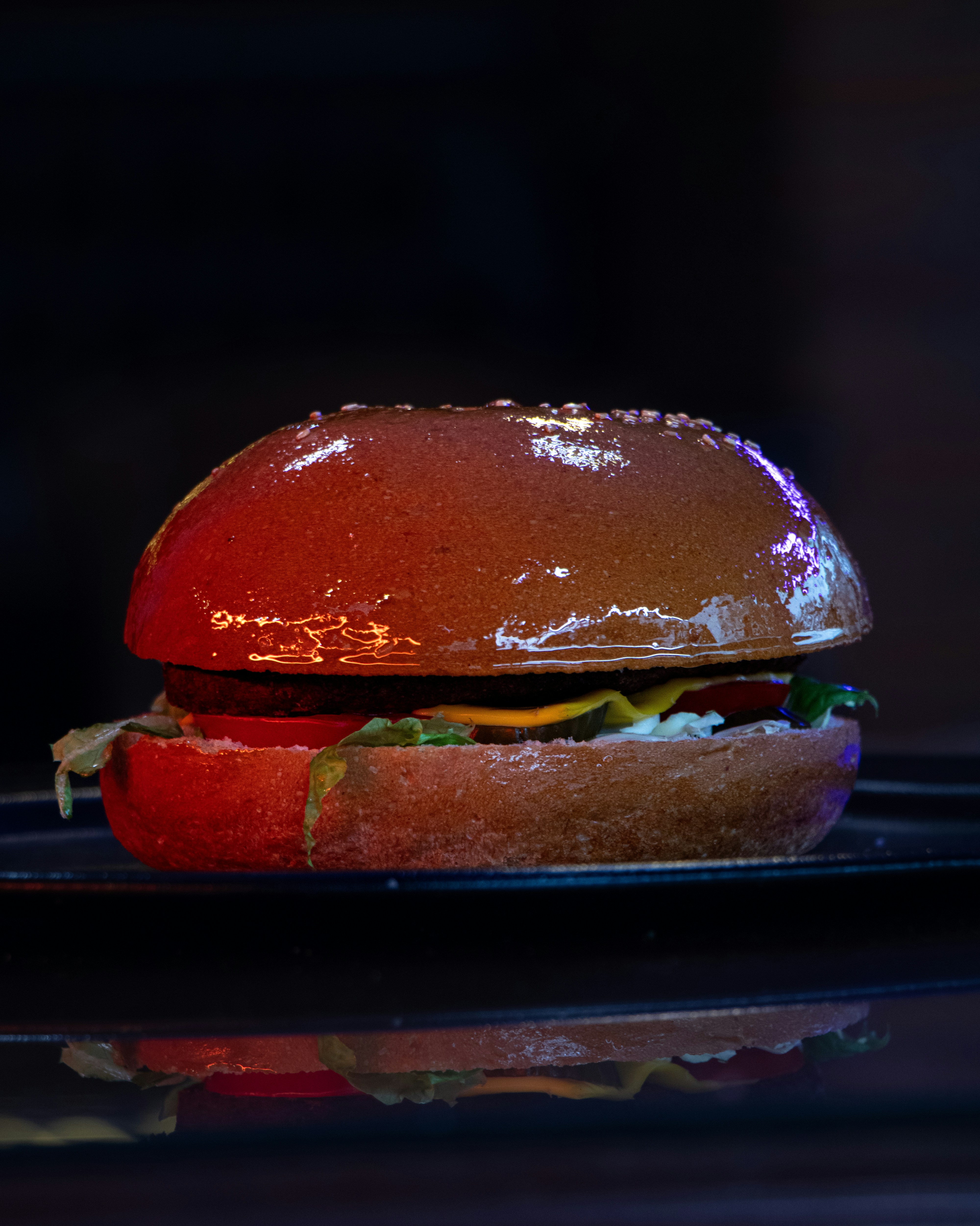 Golden crispy veg burger with fresh greens and red tomato on dark plate, moody dim lighting, deep shadows