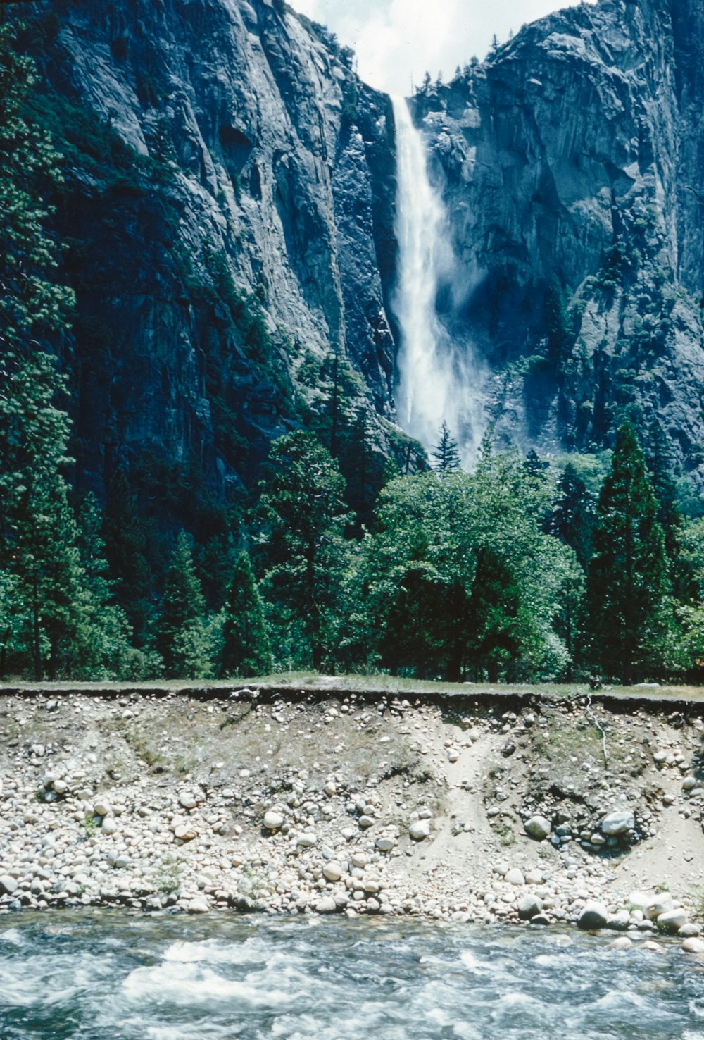 a train traveling past a waterfall next to a forest