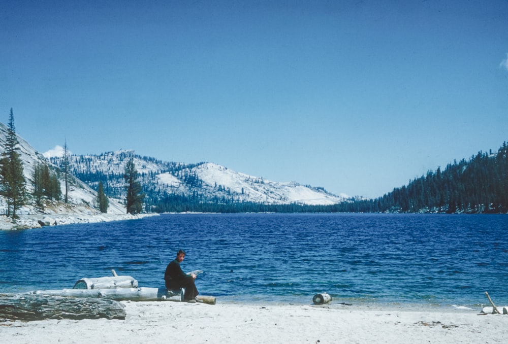 a man sitting on a beach next to a body of water