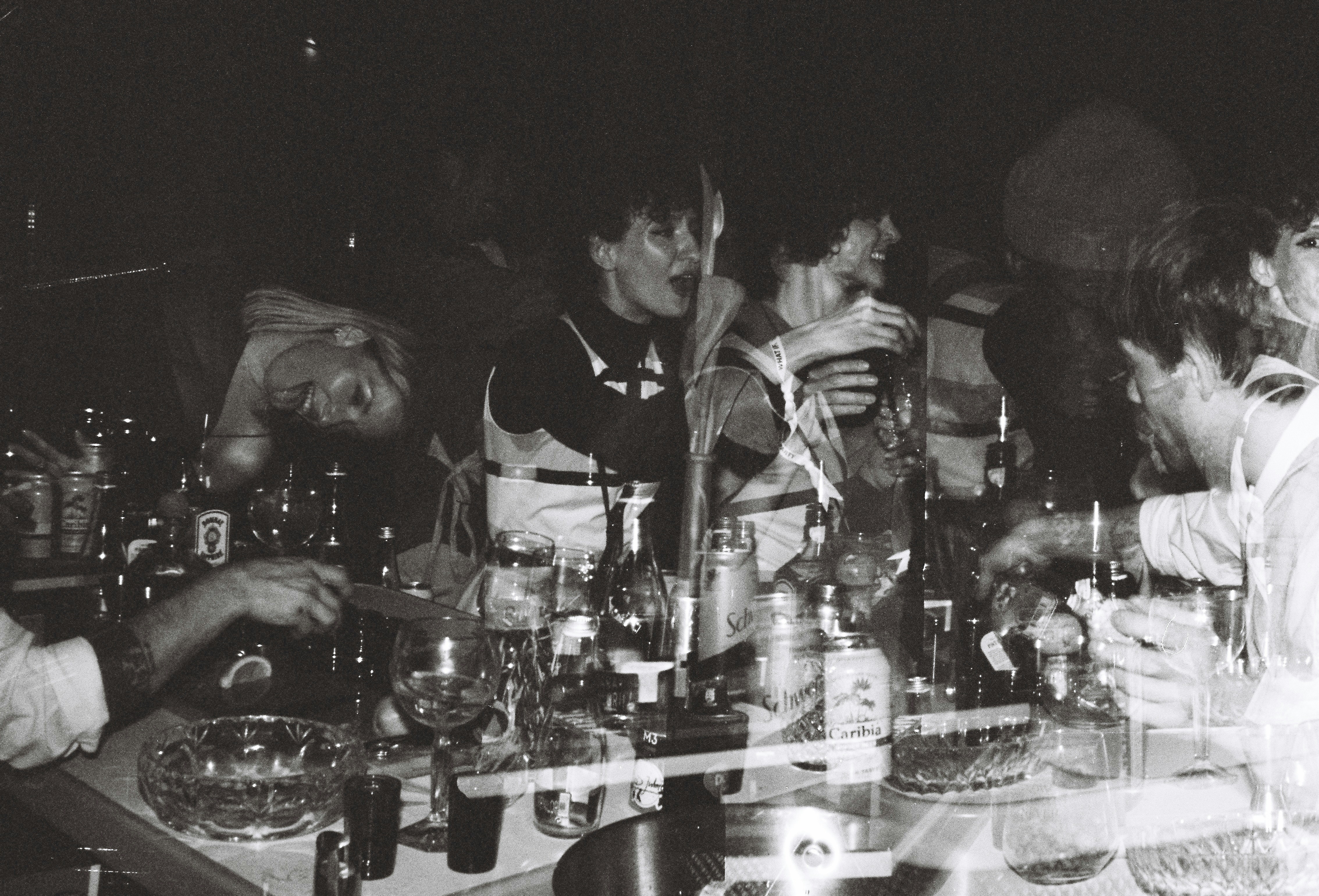 A group of men standing around a table filled with bottles and glasses ...