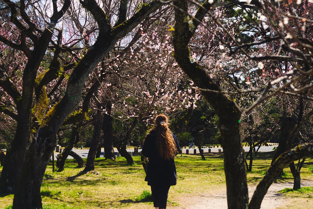 a woman walking through a park with lots of trees