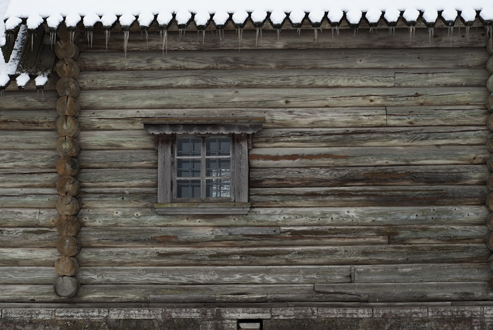 a wooden cabin with a window and snow on the roof