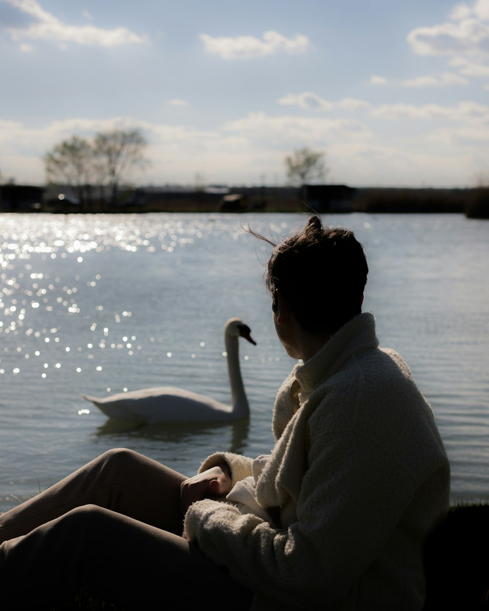a woman sitting on a bench next to a swan