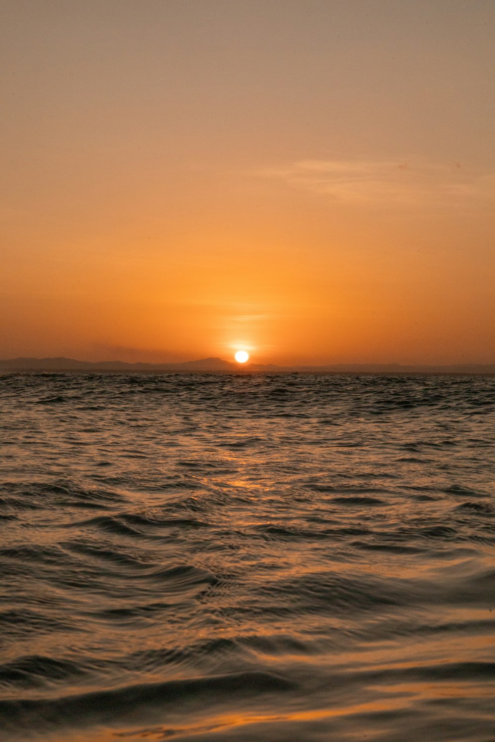 the sun is setting over the ocean with a boat in the water