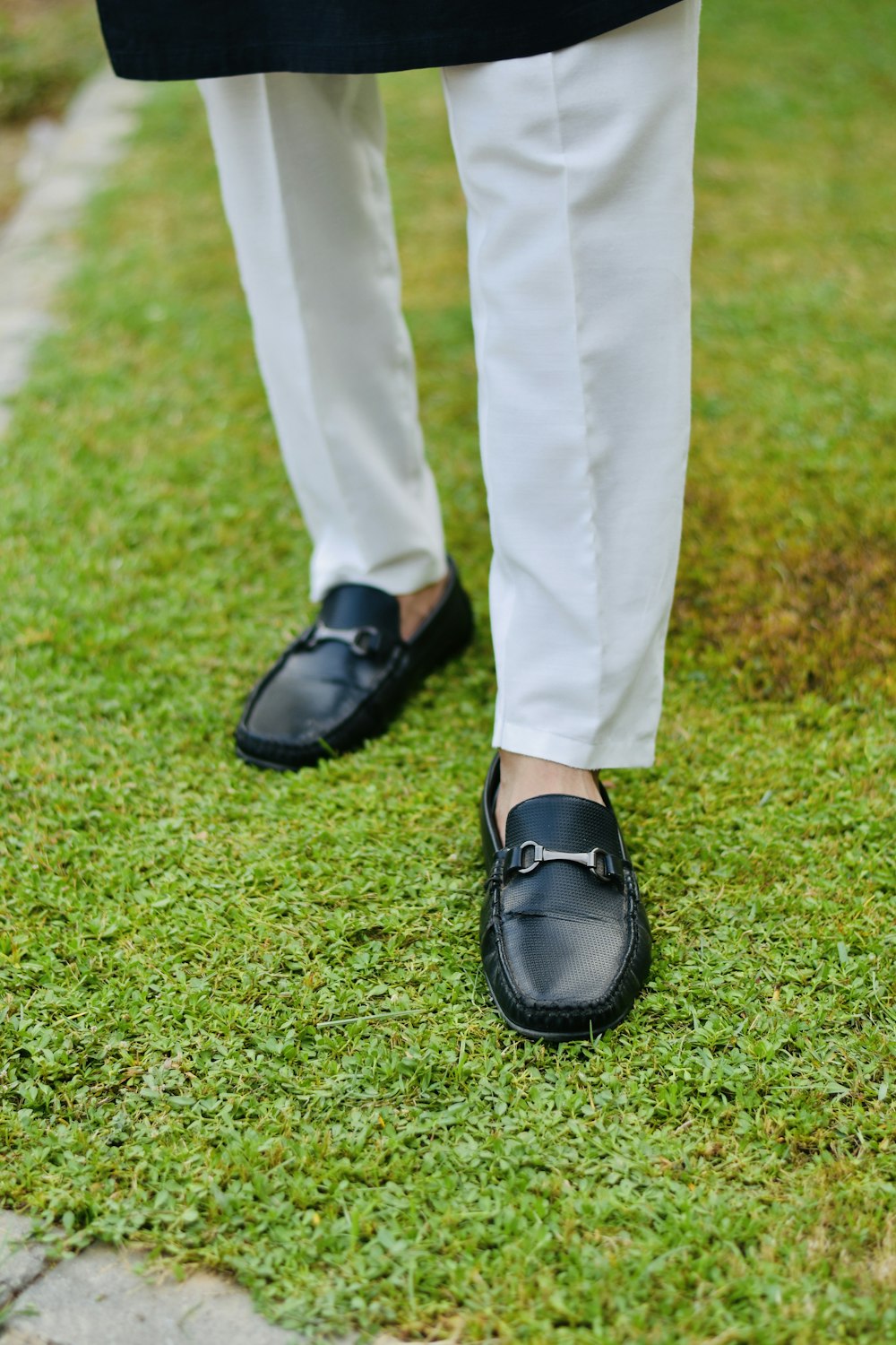 a person in white pants and black shoes standing on grass