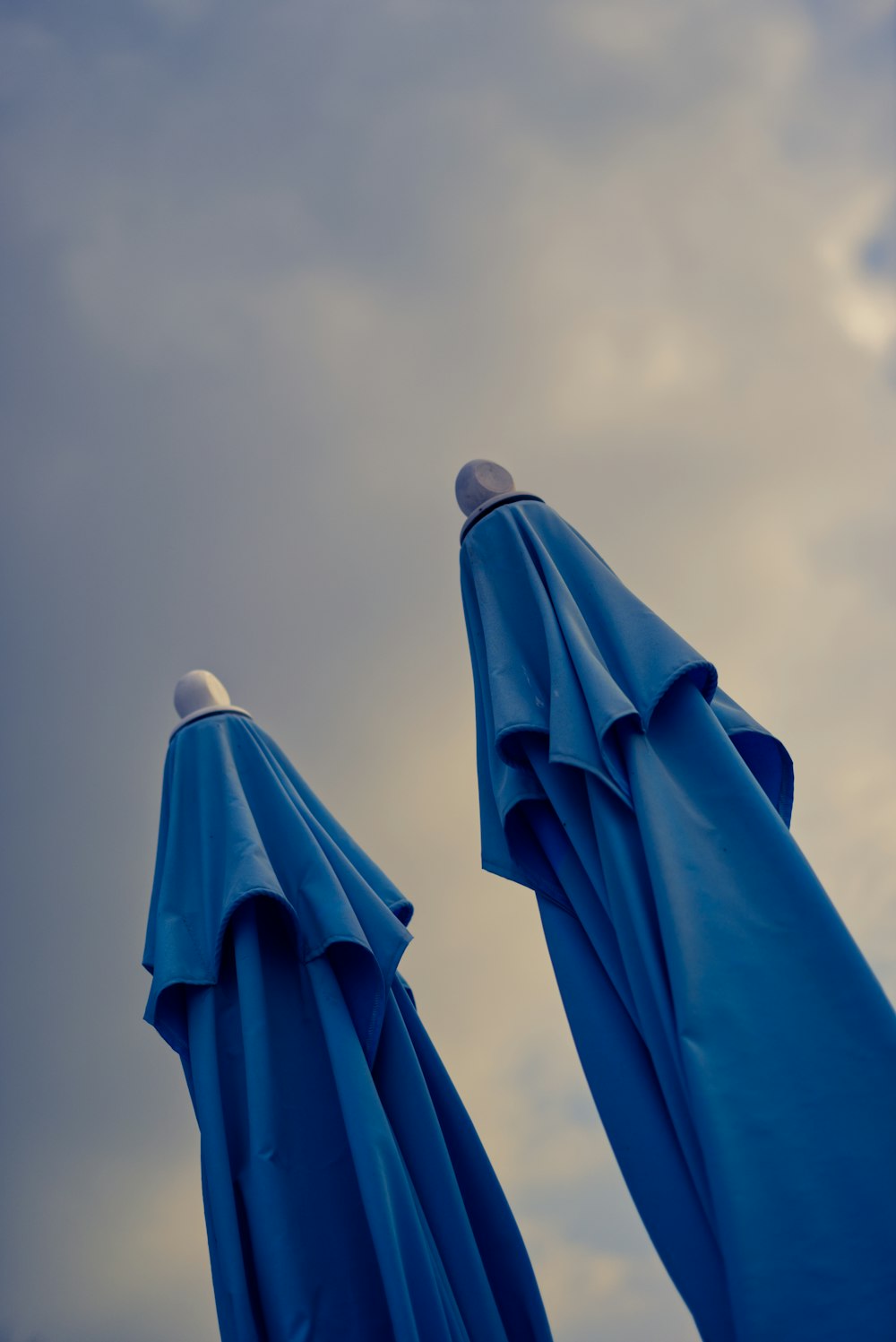 two blue umbrellas with a cloudy sky in the background