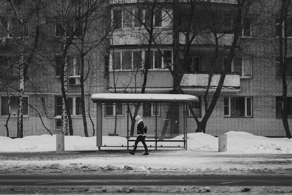a man standing in front of a bus stop covered in snow