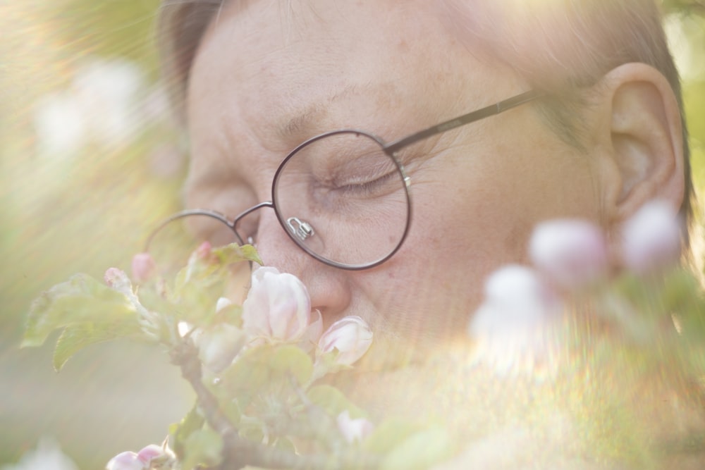 a woman with glasses is smelling a flower