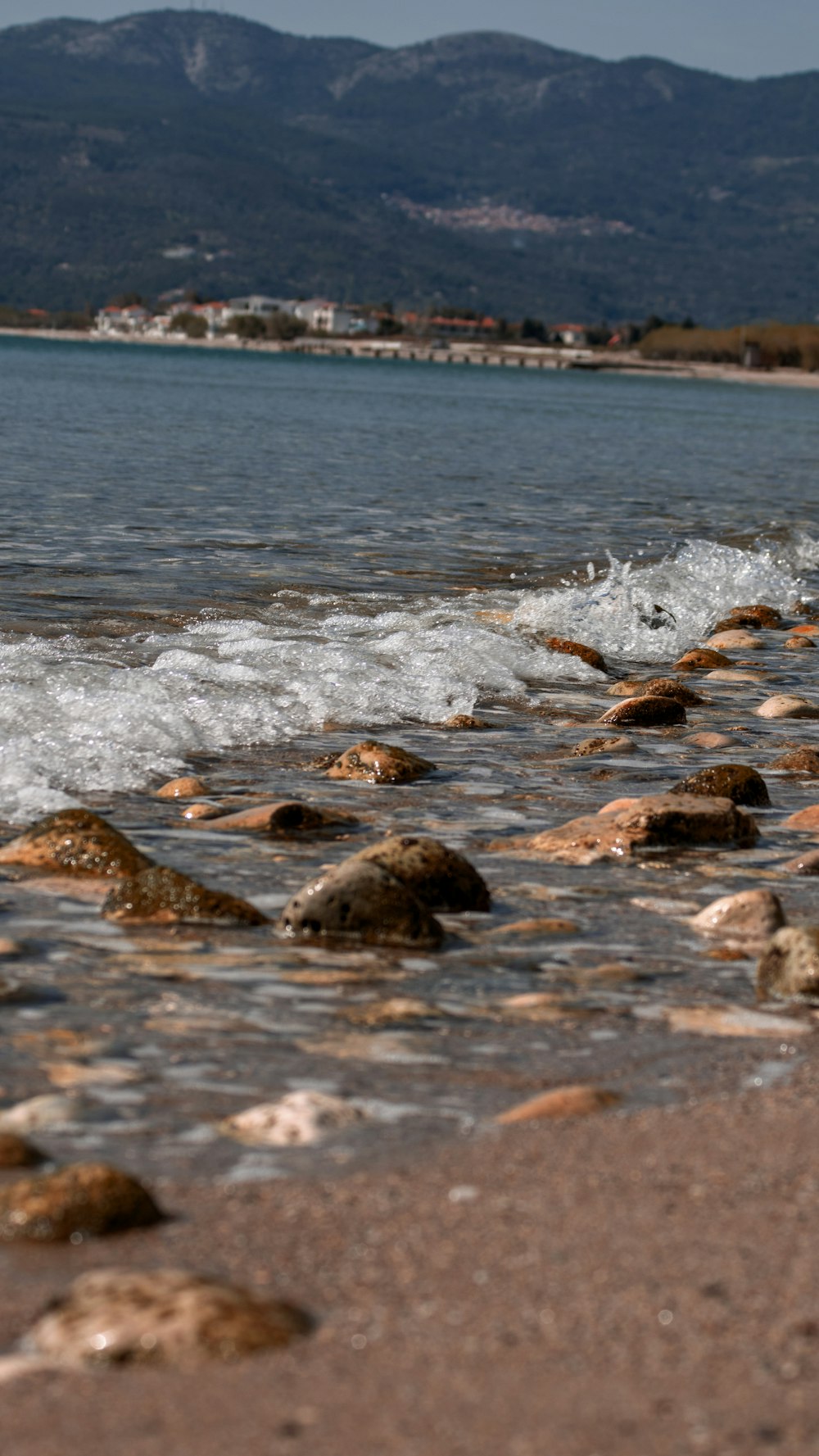 a beach area with rocks and water and mountains in the background