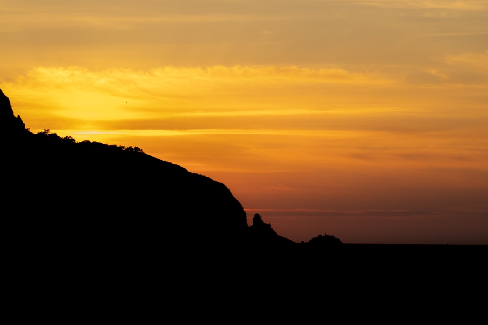 the sun is setting behind a mountain with a bird flying by