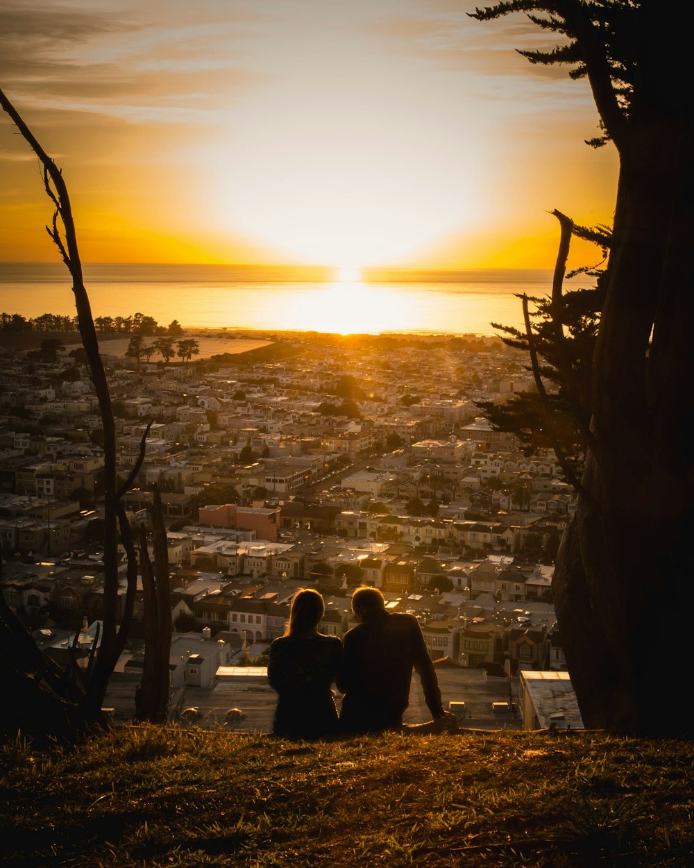 two people sitting on a hill watching the sunset