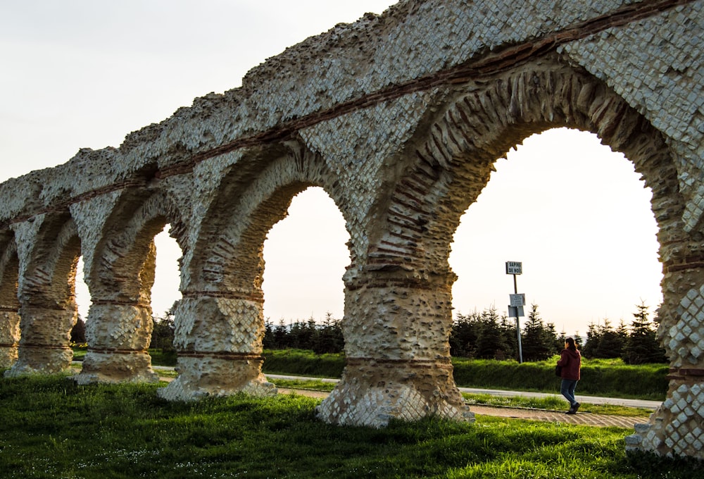 Une femme passe devant une arche de pierre dans un parc