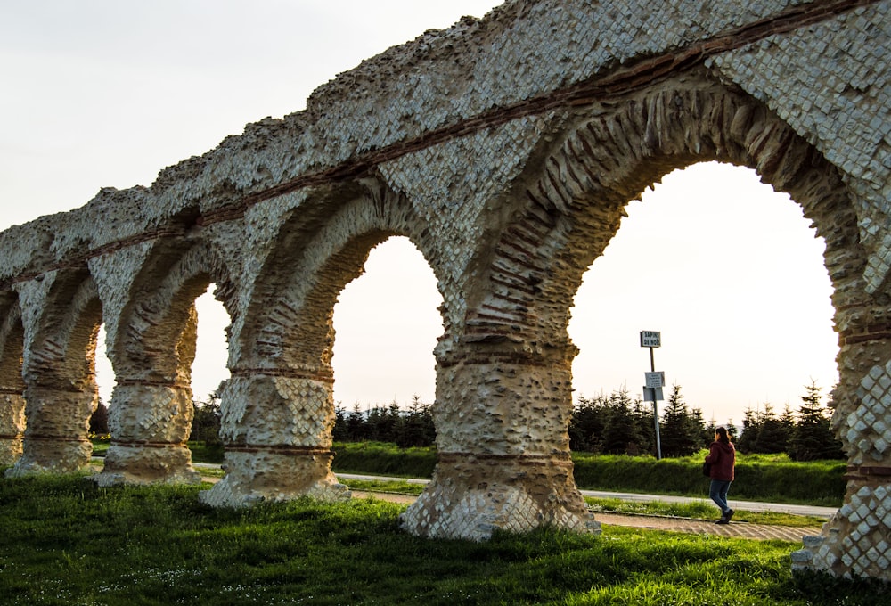 a woman walking past a stone arch in a park