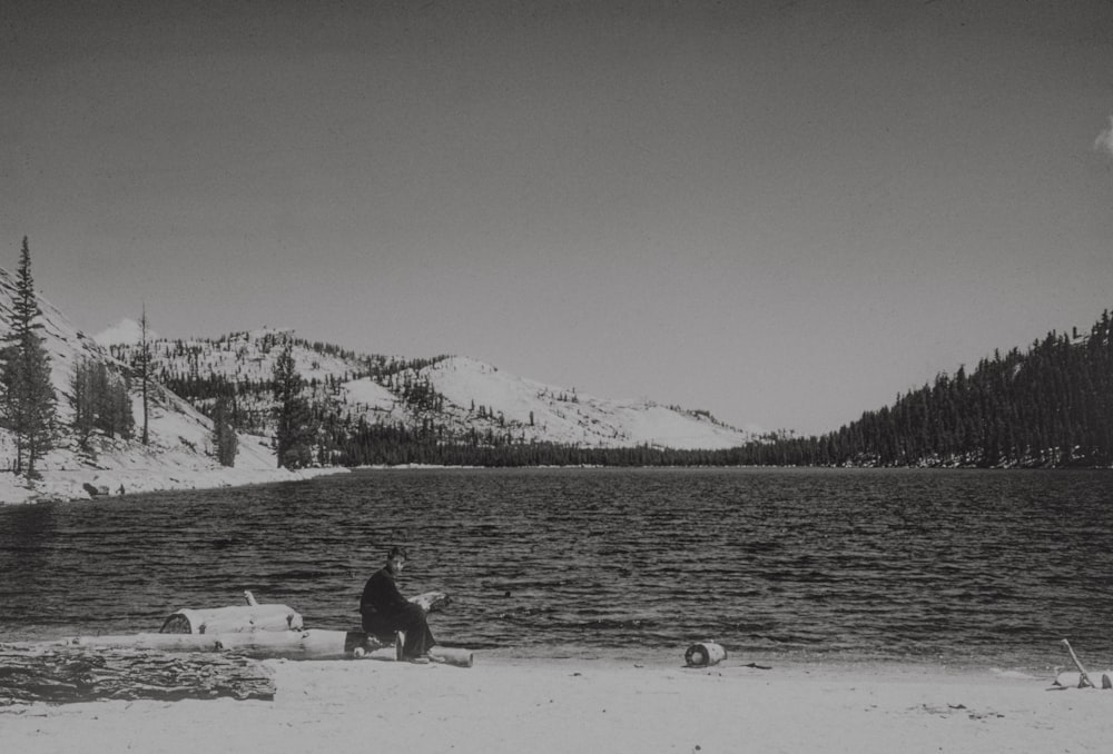a man sitting on a beach next to a lake