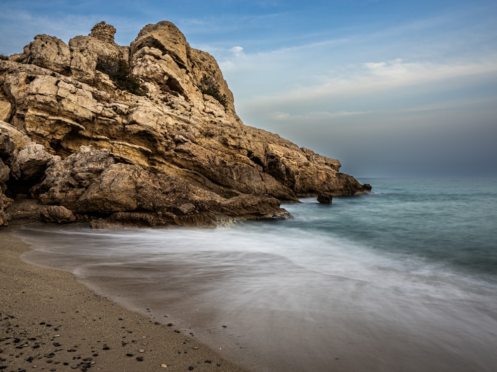 a rocky beach next to the ocean under a blue sky