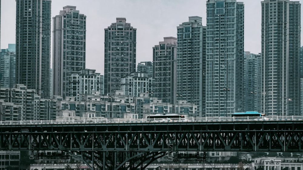 a blue bus driving across a bridge in front of tall buildings