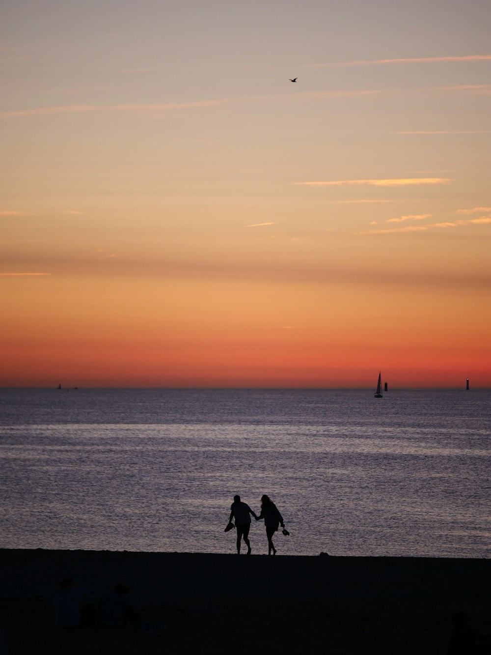 two people walking on the beach at sunset