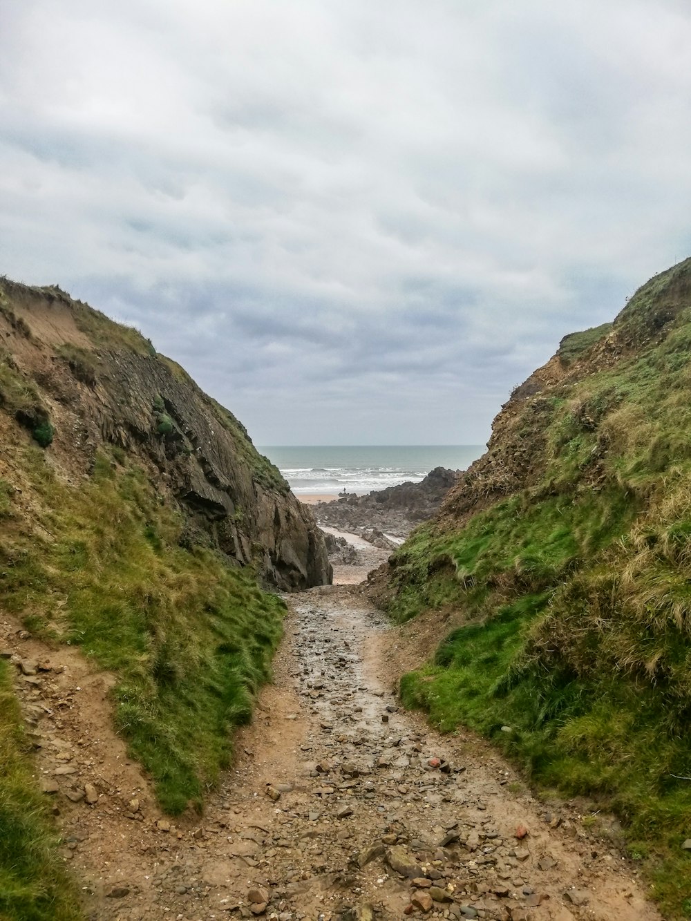 a dirt path leading to the ocean on a cloudy day