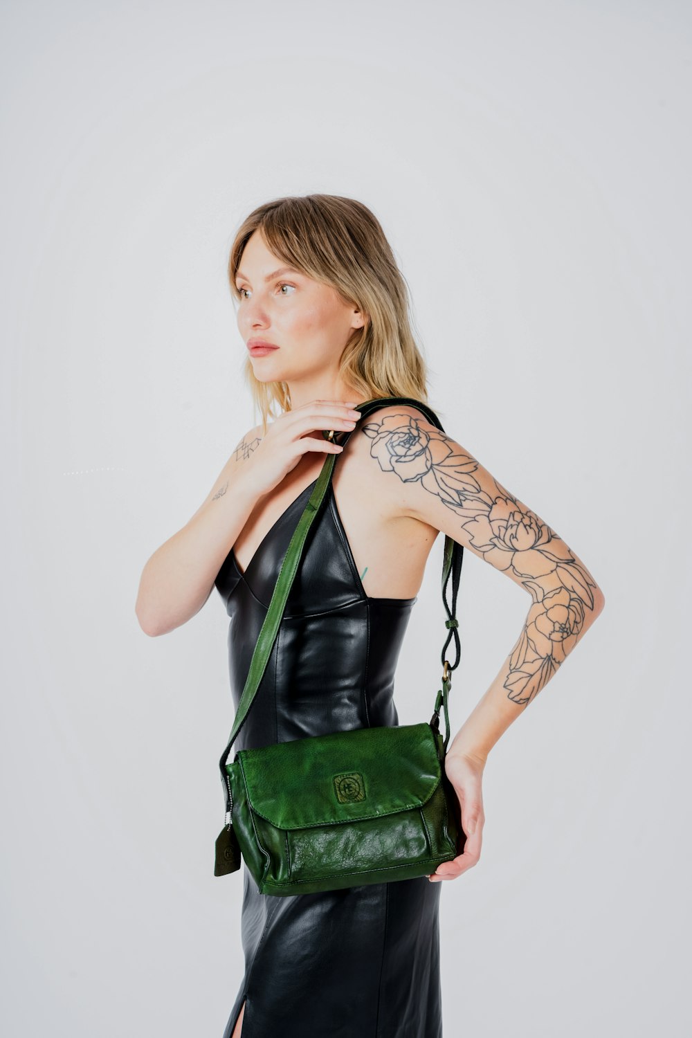 a woman in a black leather dress holding a green bag