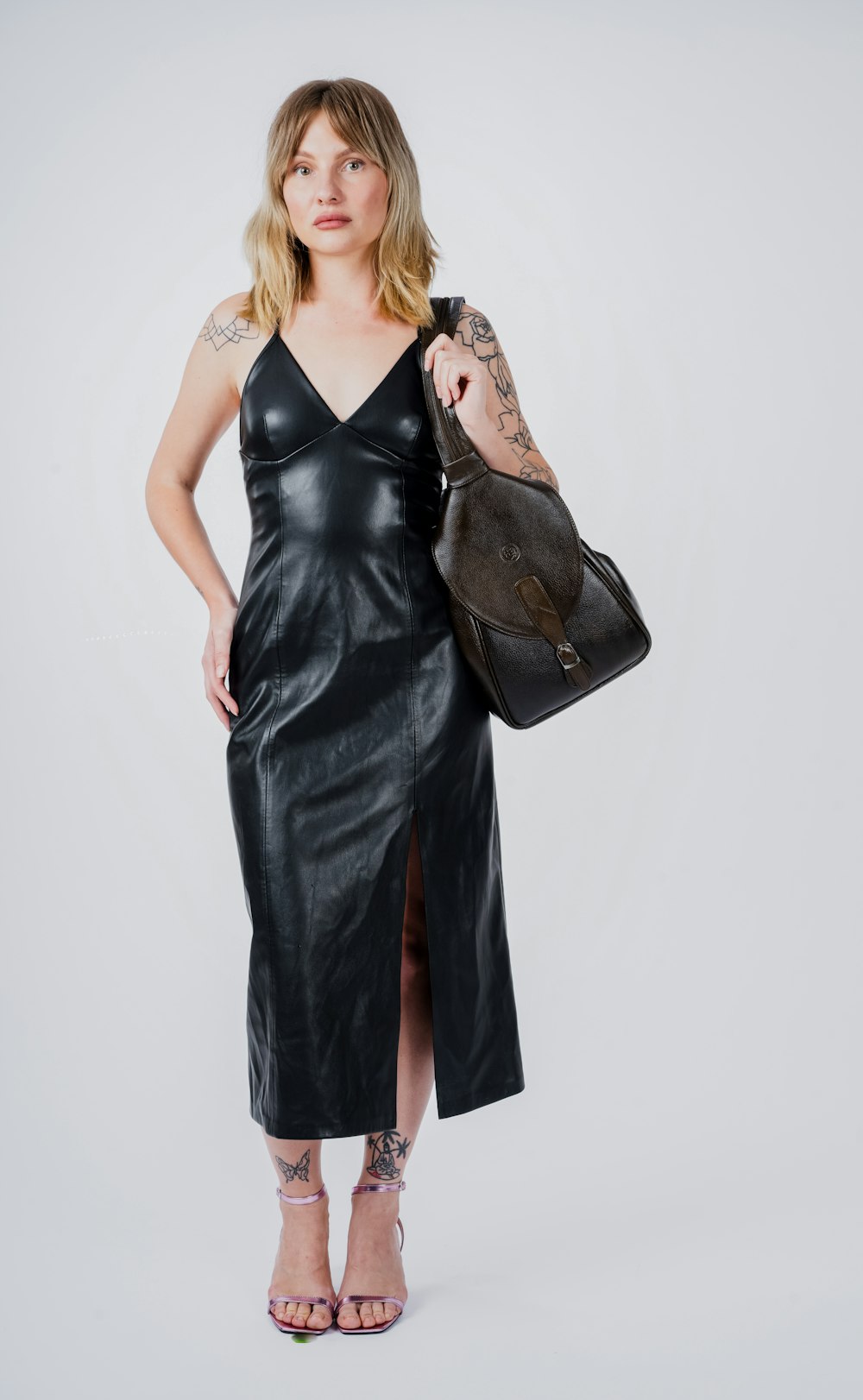 a woman in a black leather dress holding a handbag