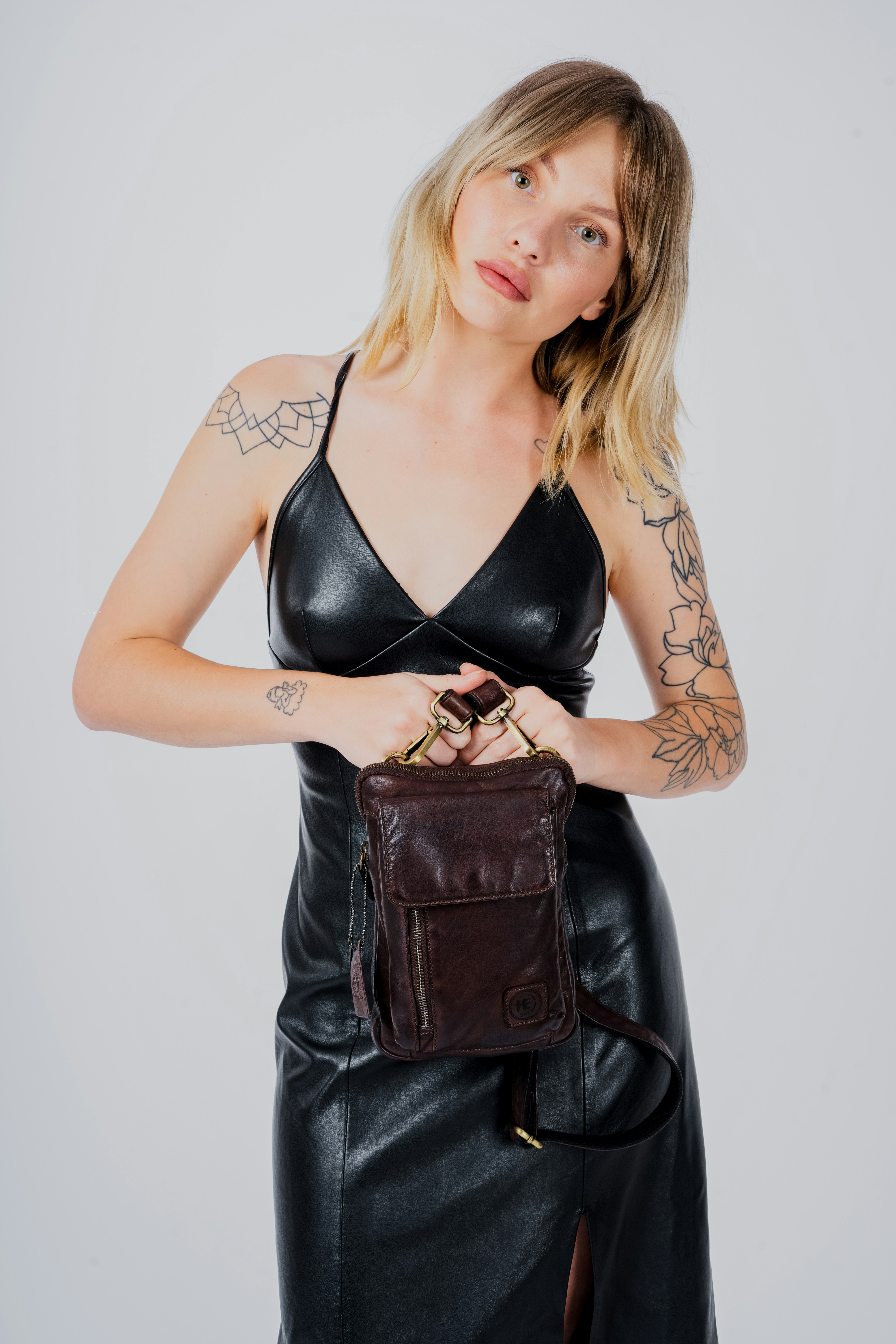 a woman in a black leather dress holding a brown purse