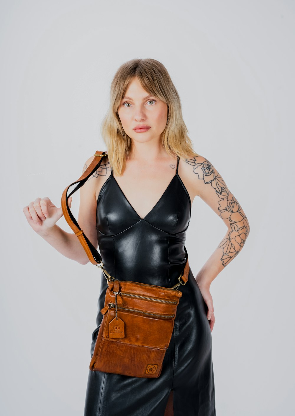 a woman in a black leather dress holding a brown purse
