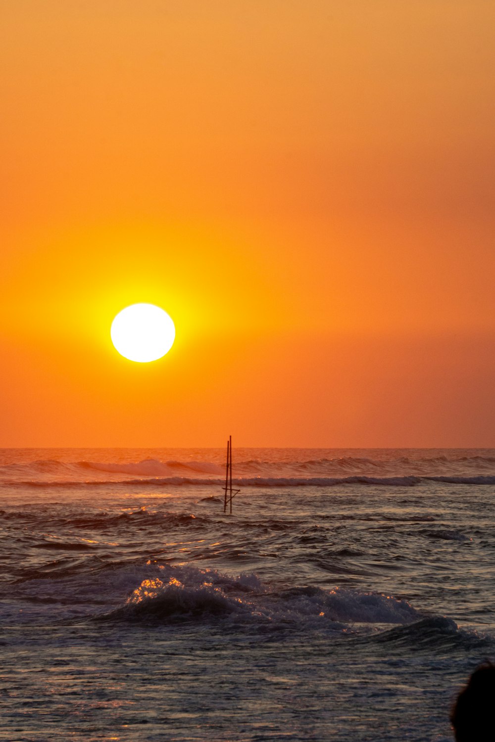 the sun is setting over the ocean with a sailboat in the water