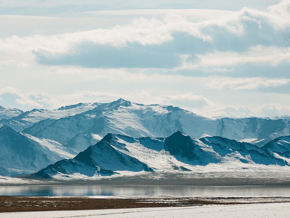 a snowy mountain range with a body of water in the foreground