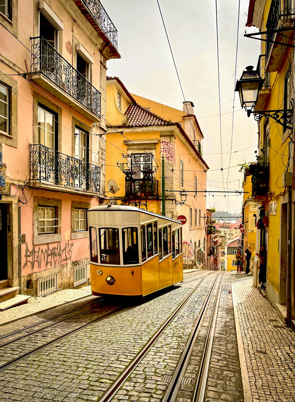 a yellow trolley car traveling down a street next to tall buildings