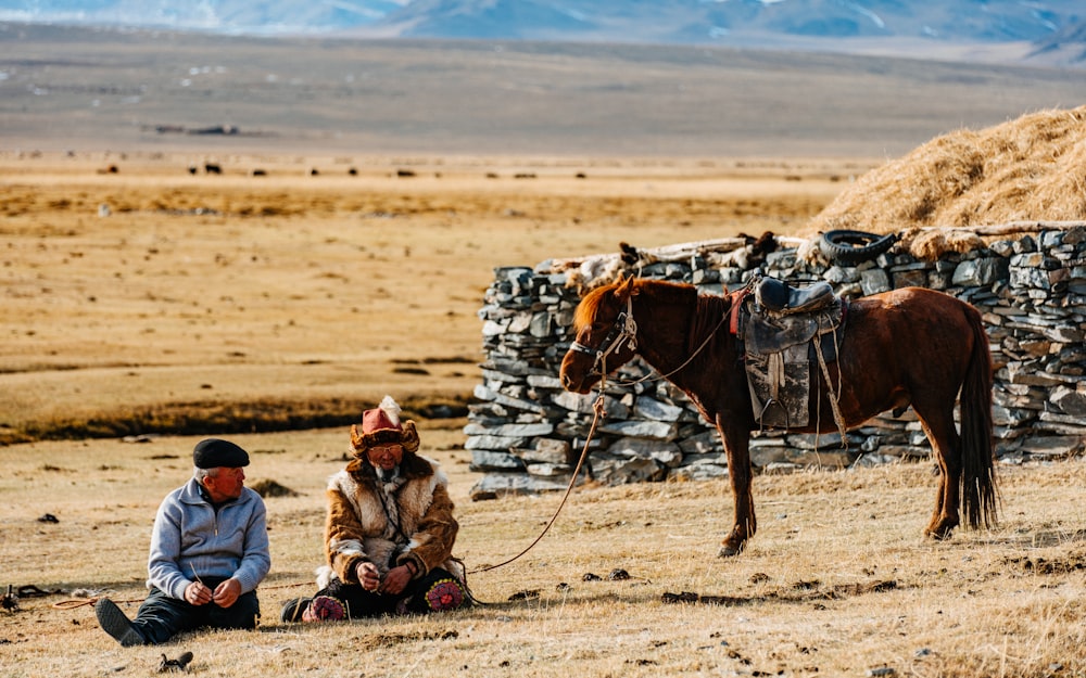 a man sitting on the ground next to a horse