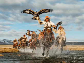 a group of people riding horses across a river