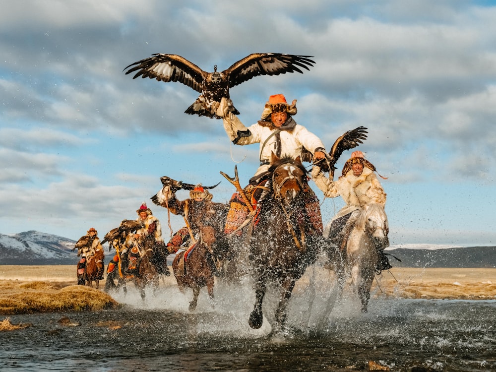 a group of people riding horses across a river