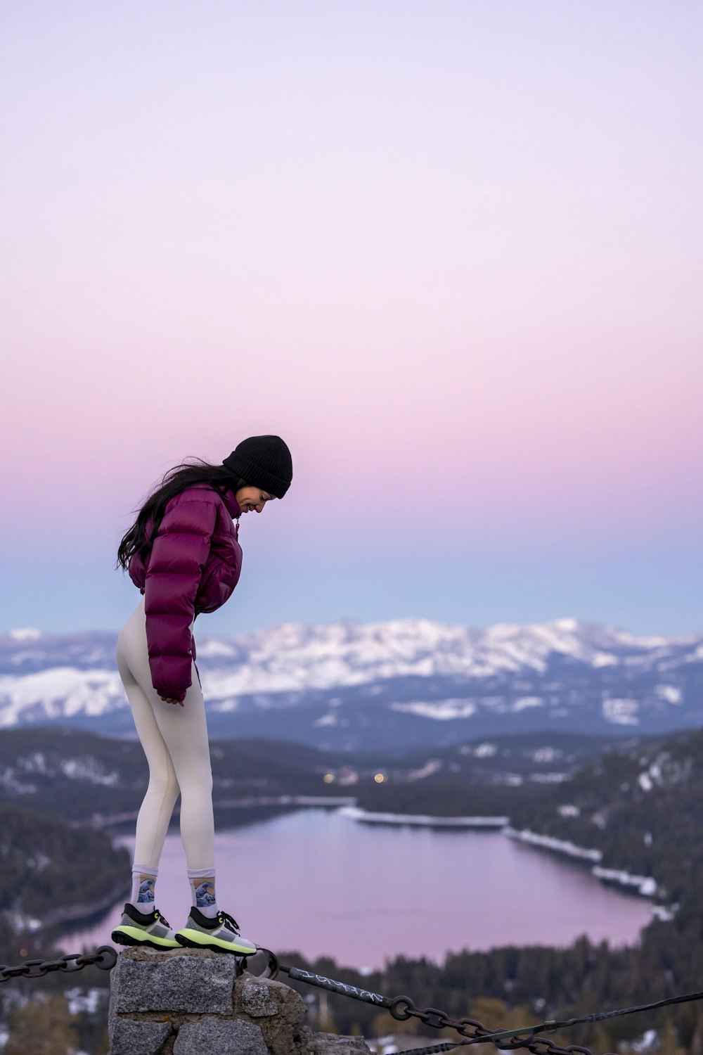 a woman standing on top of a rock next to a lake