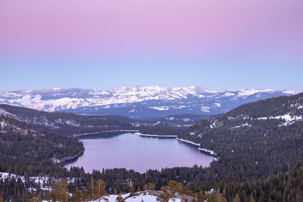 a lake surrounded by snow covered mountains under a pink sky