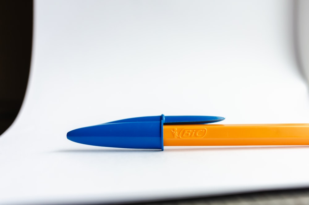 un stylo bleu et orange posé sur une table blanche