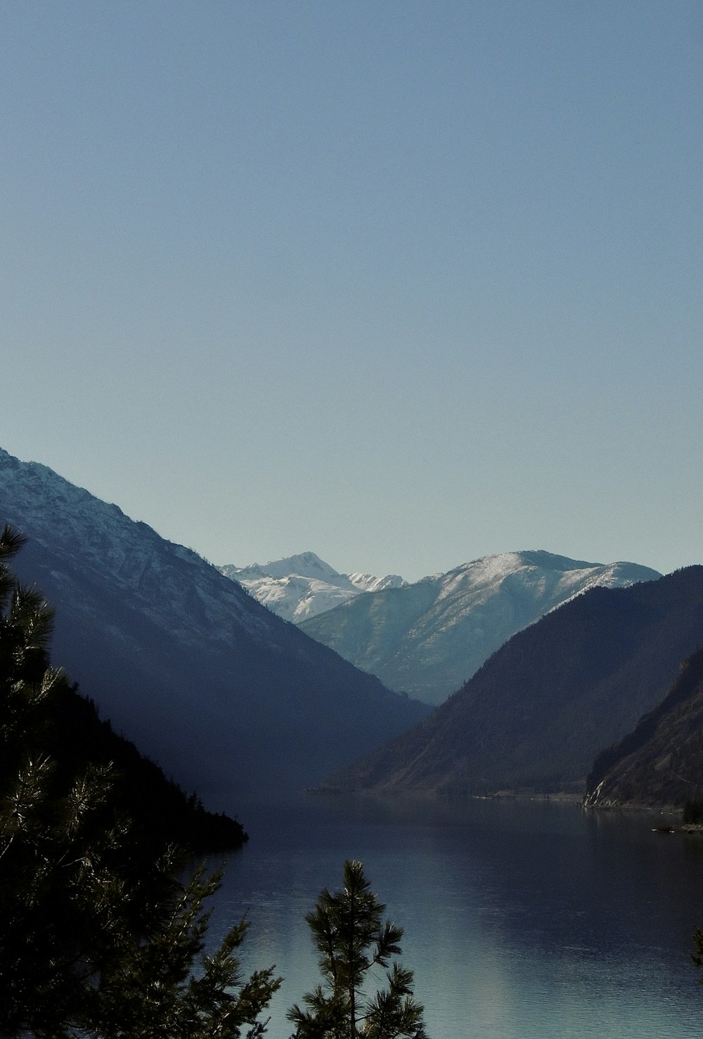 a lake surrounded by mountains and trees under a blue sky