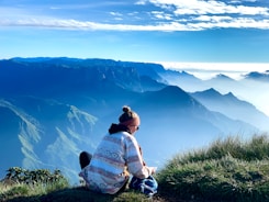 a woman sitting on top of a grass covered hill