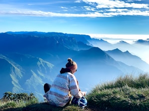 a woman sitting on top of a grass covered hill
