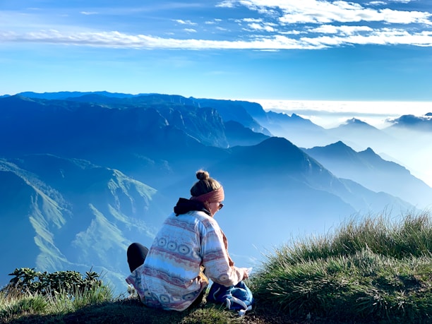 a woman sitting on top of a grass covered hill