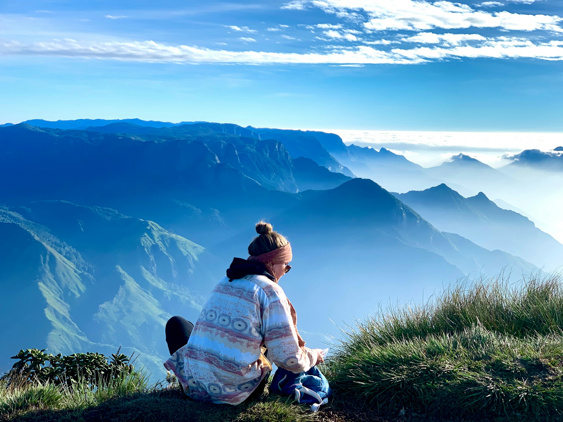 a woman sitting on top of a grass covered hill