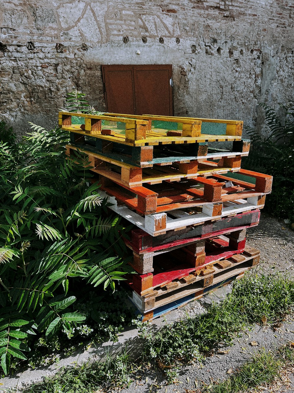 a pile of wooden pallets sitting next to a green bush
