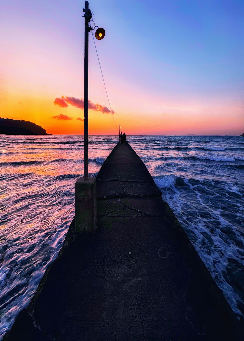 ein Lichtmast, der am Ende eines Piers neben dem Meer sitzt