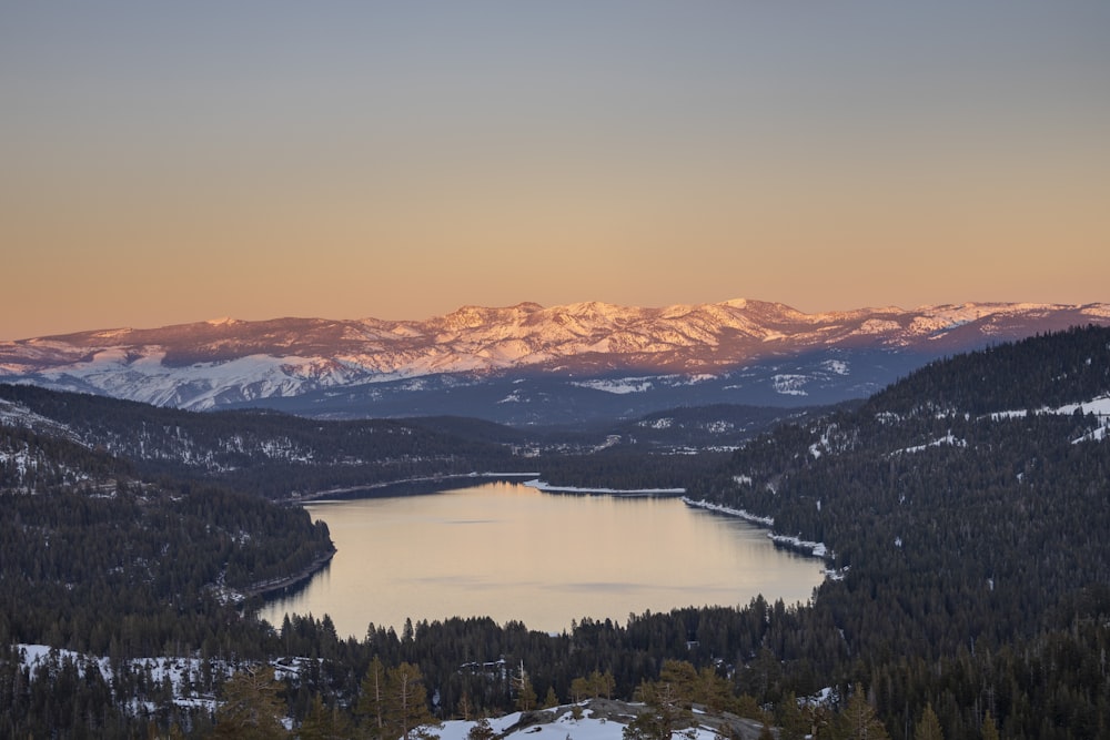 a lake surrounded by snow covered mountains at sunset